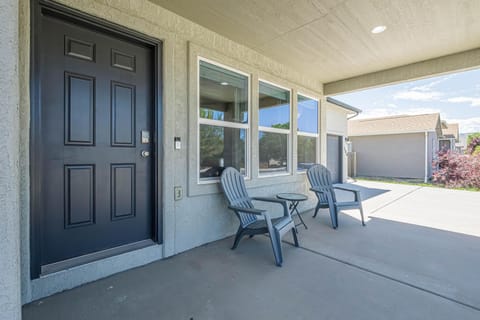 A covered front porch with two gray Adirondack chairs and a small round table on smooth concrete.