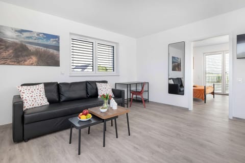 A bright living room with a black sofa, coffee table, and large windows. The space is modern and open.