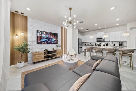 Enjoy a stylish living area with a cozy gray sectional, warm wooden accents, and modern lighting. The open layout flows into a chic kitchen, making it ideal for relaxation and gatherings with family and friends.