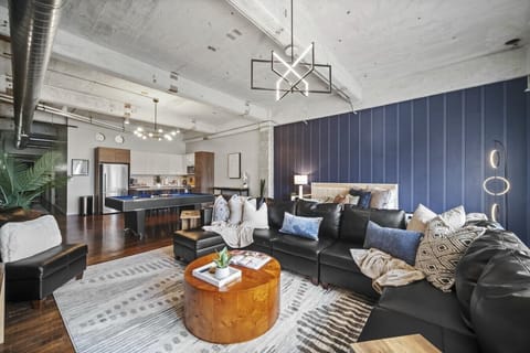 Expansive open-concept loft featuring a large black sectional sofa, pool table, modern kitchen, and stylish industrial accents.