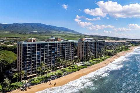 A stunning aerial perspective of Mahana Resort nestled along the golden sands of Kaanapali Beach, with lush mountains in the background.