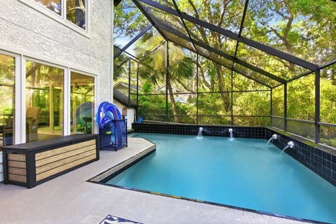 The full pool area showcases the waterfall jets, poolside storage bench, blue floaties at the ready, and a lush canopy of trees through the screen — total seclusion.