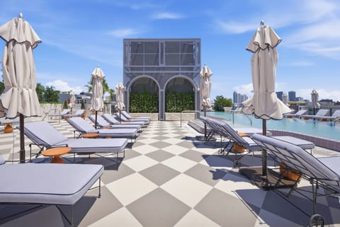 Experience our stunning rooftop terrace, featuring stylish lounge chairs and elegant umbrellas, perfect for sunbathing or enjoying a refreshing drink while soaking in breathtaking panoramic views and chic checkerboard tiles.