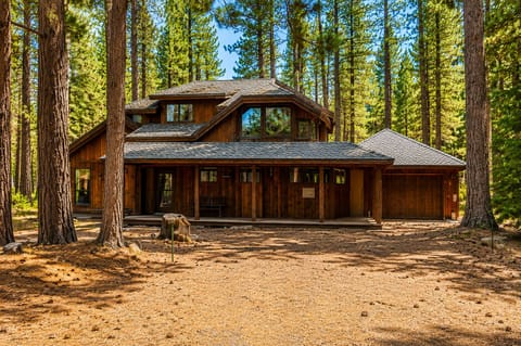 A two-story wooden lodge surrounded by towering pines in a tranquil forest setting.