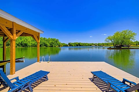 Dock & Boathouse - Blue loungers face an expansive lake view from the dock, the boathouse roofline shading one side over mirror-calm water.