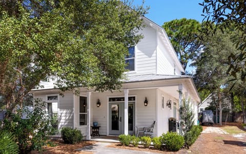 Charming coastal-style home with a shaded front porch and lush greenery all around.