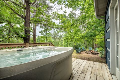 The property features a bubbling hot tub on a spacious deck surrounded by lush wooded scenery, with a fire pit area and outdoor seating nestled among towering trees for peaceful mountain relaxation.