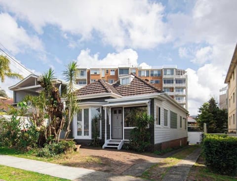 Welcome home to this charming weatherboard cottage, featuring a tiled roof, lush front garden greenery, a paved entryway, and classic character set against a sunny sky backdrop.