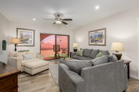 Living room with wood-look tile flooring, gray and beige sofas, Southwestern artwork, and sliding glass doors to balcony.