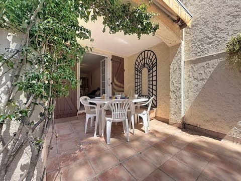 Un déjeuner d`été à l`ombre: la table dressée sous la vigne grimpante, le treillis noir et le store créent une alcôve provençale où se racontent des soirées longues et tranquilles.