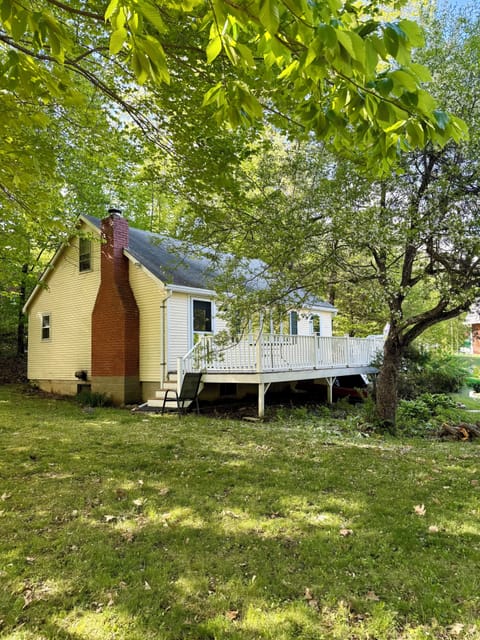 Charming cottage nestled beneath mature trees, offering a peaceful retreat with a brick fireplace and private deck surrounded by lush greenery.