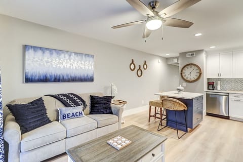 Coastal textures and deep indigo accents create a calm, open living space. Weathered wood and woven seating ground the room in comfort, while soft overhead light highlights the clean lines of the kitchen island.