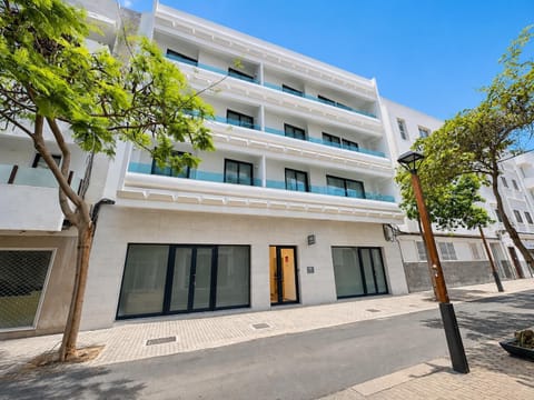 A modern white apartment building with stylish balconies on a sunny city street.