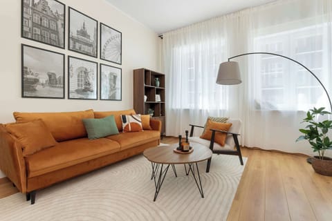 A stylish living room with an orange sofa and seating area. Large windows fill the space with natural light.