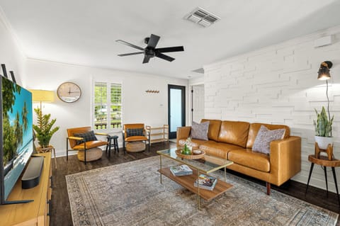 Sink into the buttery leather sofa and unwind in your stylish living room, where mid-century charm meets modern comfort beneath a cooling ceiling fan.