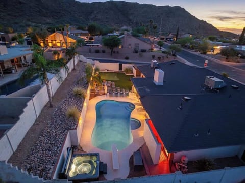 Aerial view captures this vacation retreat at twilight, with mountain backdrop, private pool, hot tub, and spacious yard lit warmly against the desert neighborhood.