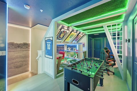 Have fun in a soccer themed game room with a foosball table, framed jerseys, gaming chairs, soccer decor, green LED lighting, and stadium-inspired details, creating an exciting space for family entertainment during vacation.