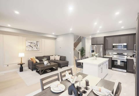 Modern open-plan space with plush sectional, stylish dining setup, sleek kitchen with stainless steel appliances, island seating, decor accents, and soft lighting.
