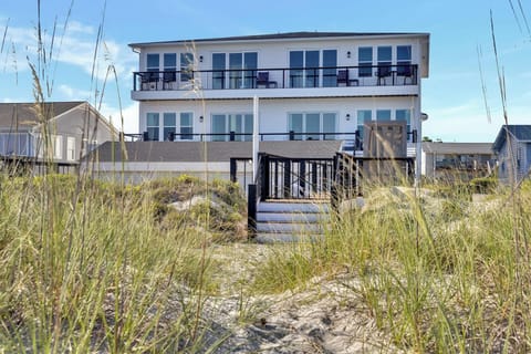 A beachfront vacation home with direct access through natural dunes, featuring multiple balconies overlooking the shore and spacious outdoor areas for gathering.