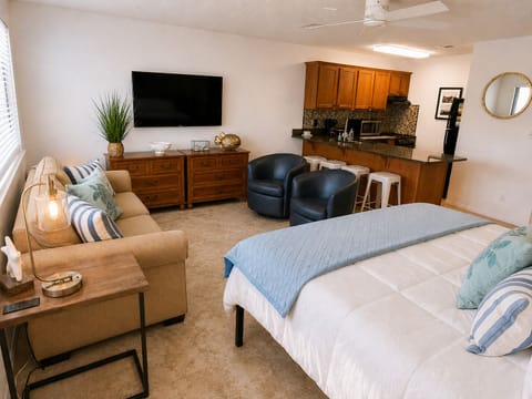 Bright open-concept studio with full kitchen, TV, and cozy seating