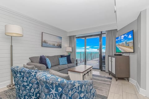 Bright coastal-inspired living room featuring comfortable seating, Smart TV, and floor-to-ceiling balcony access with breathtaking oceanfront views.
