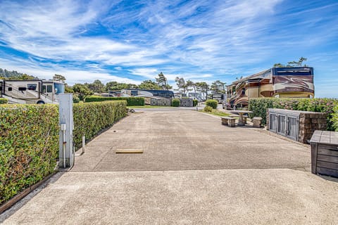 Spacious RV parking area with manicured hedges, surrounded by coastal trees and blue skies, providing a scenic retreat for your vacation stay.