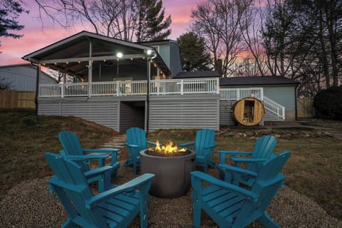 Twilight waterfront view with a fire pit, outdoor seating, covered deck and barrel sauna.