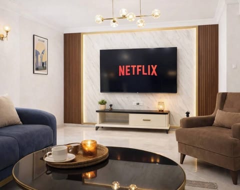 Bright, stylish living room with a large Smart TV, soft lighting and comfortable seating. Ideal for unwinding after a day in Agadir, whether watching Netflix, enjoying a coffee or relaxing in a calm, modern space designed for comfort and ease.