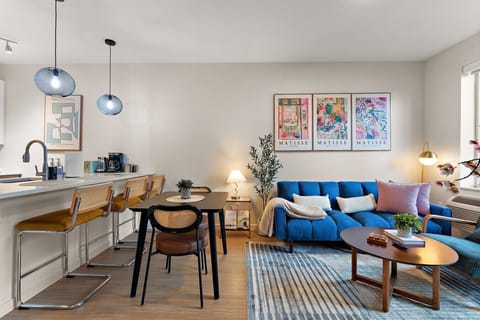 Bright open-concept living and dining area with cozy seating, stylish decor, and a fully equipped kitchen nearby.