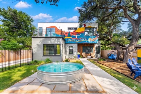 Cool off in the circular stock tank pool of this vibrant modern getaway, featuring a eye-catching colorful mural, a shaded yard with mature trees, and inviting outdoor seating areas.