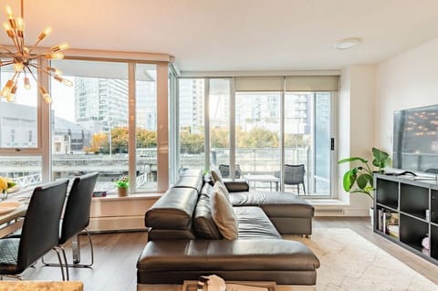 Bright downtown Vancouver living room with floor to ceiling windows, TV, and private balcony access.