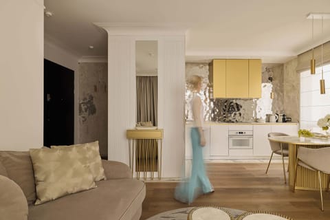Salon zachwyca jasną kolorystyką oraz złotymi akcentami, które nadają wnętrzu luksusowy charakter. Znajduje się tu wygodna, rozkładana sofa, idealna do codziennego relaksu, jak i jako dodatkowe miejsce do spania. Naprzeciwko umieszczono telewizor.