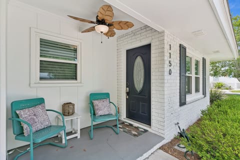 The property entrance features white brick siding with black shutters, decorative address numbers, and a welcoming porch area with ceiling fan.