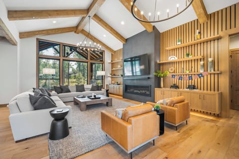 Sink into plush seating surrounded by vaulted ceilings and warm wood tones, where your evening unwinds by the fireplace beneath forest views through expansive windows.