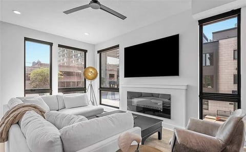 Modern living room with large windows, a wall-mounted television, and a sleek electric fireplace.