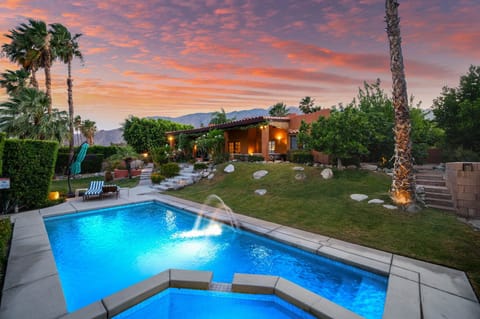 Stunning desert retreat captured beneath a vibrant sunset sky, featuring a sparkling pool surrounded by lush landscaping, palm trees, and mountain views—perfect for a serene getaway.