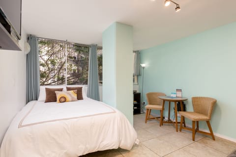 Wake up to garden views from your cozy bed, then enjoy morning coffee at your private table. The soothing mint accent wall and natural wicker chairs create a peaceful retreat.