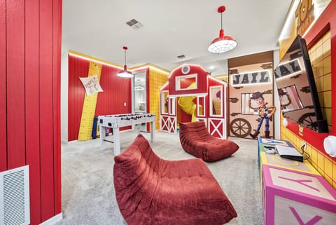 Discover a lively playroom adorned in bright red and yellow, complete with inviting bean bag chairs for relaxation. A charming barn-style playhouse and playful decor promise endless fun for kids and the young at heart.