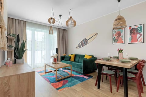A bright and cozy living room with a comfortable sofa and dining area. Large windows fill the space with natural light, creating a welcoming atmosphere.