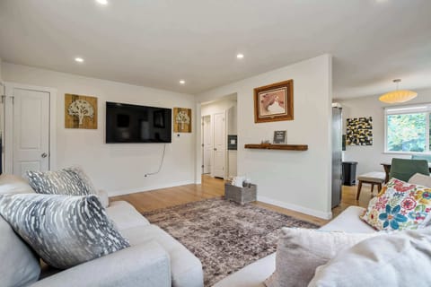 From this angle, the room settles into movie-night mode: a wall mounted Smart TV, a rustic floating shelf overhead, and enough open floor for kids to sprawl before the day winds down toward the bedrooms upstairs.