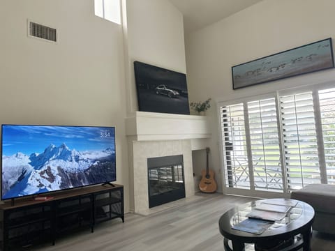 Relax in style in this welcoming living space, featuring a classic fireplace mantel, a large flat-screen TV, elegant plantation shutters, and plenty of natural light.