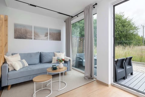 A cozy living space featuring a blue sofa, a small coffee table, and large glass doors opening to the outside. Sunlight fills the room, highlighting the clean, modern aesthetic.