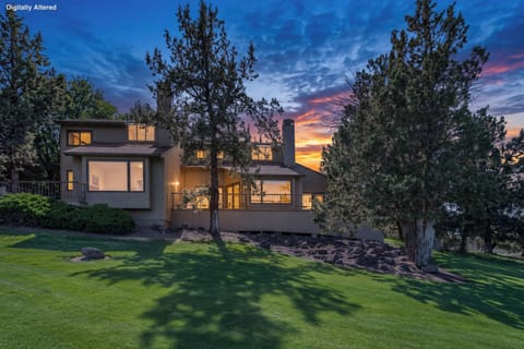 Modern retreat set on manicured lawns beneath towering pines, framed by vibrant sunset skies. The property offers a peaceful natural setting with mature trees and open green spaces.