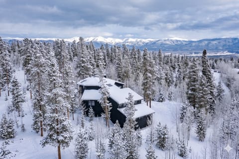 This winter mountain property sits nestled in a pristine snow-covered forest with stunning views of distant peaks and valleys, offering a serene alpine escape surrounded by nature's beauty.
