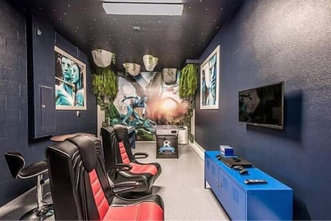 Discover a lively entertainment lounge with bold blue walls and sleek black and red gaming chairs, creating a dynamic atmosphere. Delight in the eclectic art and clever lighting, perfect for fun evenings with friends or family.