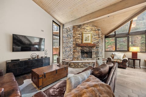 Relax in the spacious living room featuring soaring wood-beamed ceilings, a floor-to-ceiling stone fireplace, comfortable seating, a Smart TV, and large windows that fill the space with natural light.