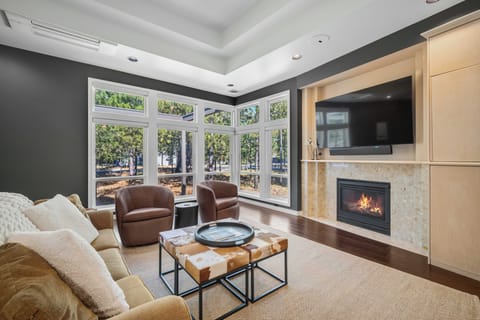 Settle into plush seating beside a warm fireplace, where sunlight streams through expansive windows overlooking peaceful wooded surroundings. Your perfect retreat for relaxation awaits.