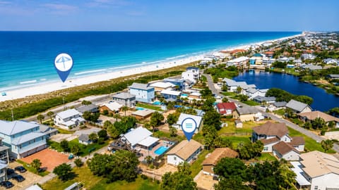 Aerial view of a beachfront coastal community with palm trees, residential properties, and a tranquil inland waterway alongside pristine sandy shores and turquoise ocean waters.