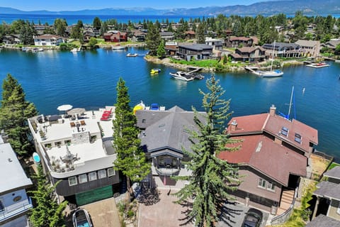 Lakefront neighborhood with private docks, boats, and homes surrounded by sparkling blue water, evergreen trees, and distant mountain peaks.