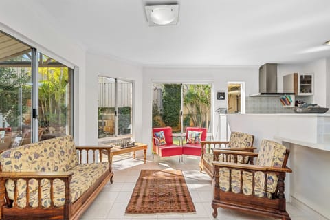 Bask in the abundant natural light of this airy lounge space, featuring classic wooden seating, vibrant red accent chairs, and expansive glass doors that beautifully frame the lush outdoor garden.